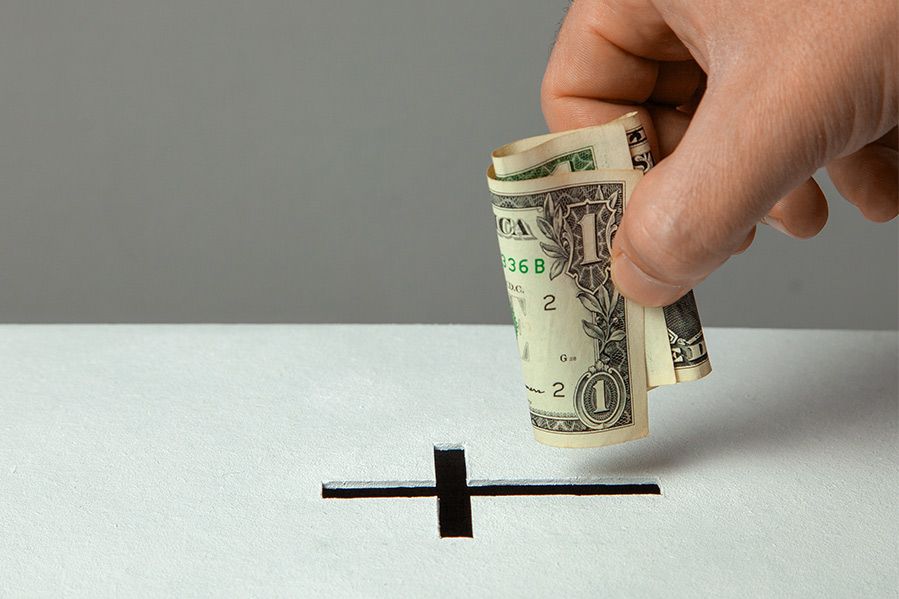 hand dropping cash into cross shaped piggy bank