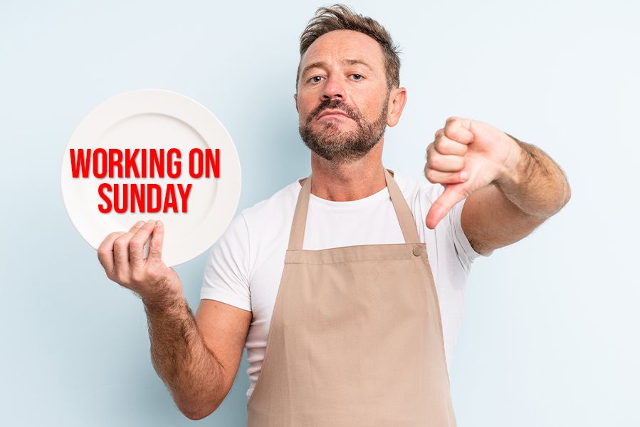 cook holding a plate that says 'working on sunday' while making a thumbs down gesture