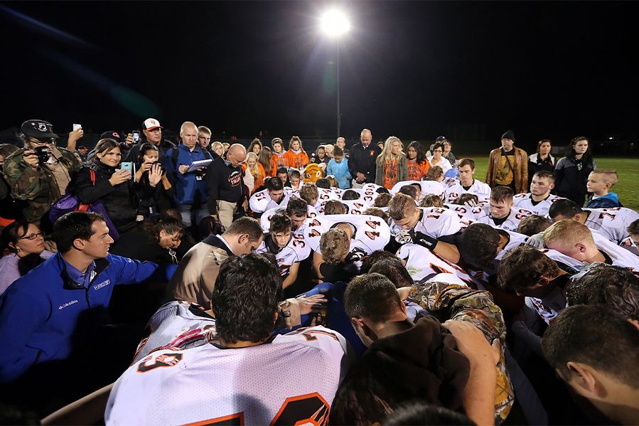 football coach joe kennedy praying with team on 50-yard line