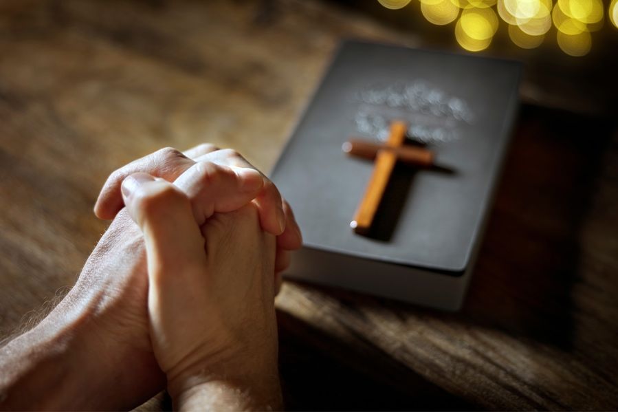 hands clasped in prayer over Christian Bible