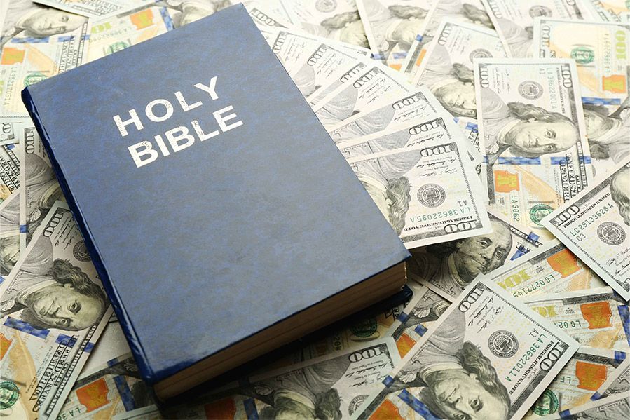 holy bible laying on pile of hundred dollar bills