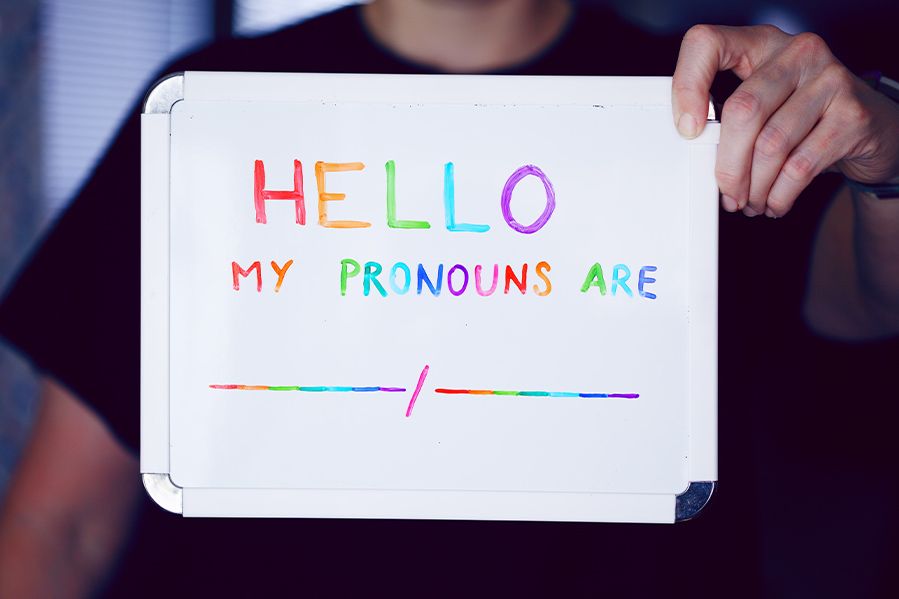 man holding up colorful pronoun sign