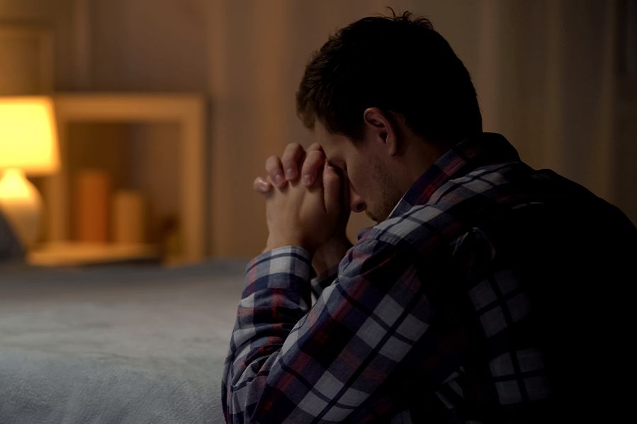 man with hands clasped in prayer during evening at bedside