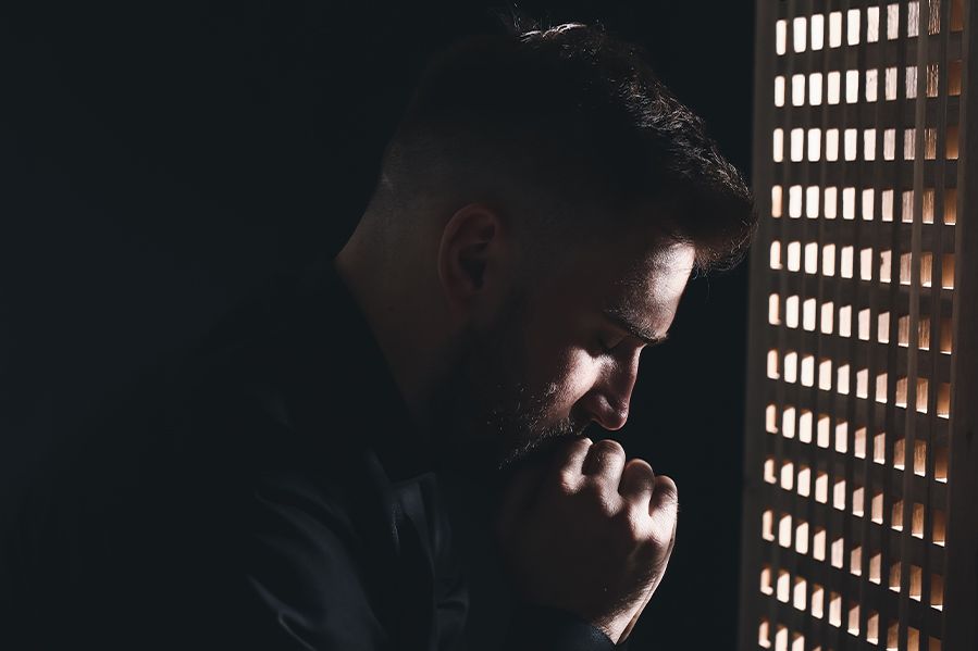 priest praying in confession booth