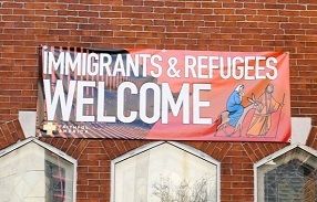 A sign on a brick church indicating that immigrants and refugees are welcome