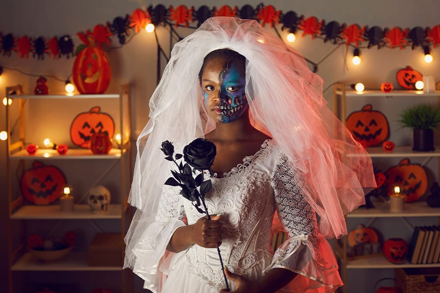 A woman wearing a veil in spooky face-paint holding a black rose