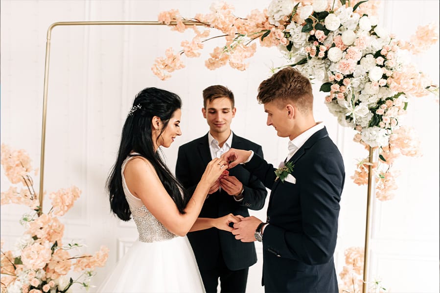 A newlywed couple and officiant during a ceremony with flowers inside